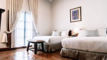 A hotel room with two beds, a bench, a window with curtains, and a framed picture on the wall.
