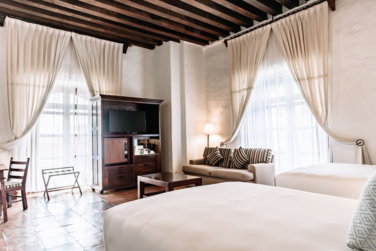 A hotel room with a large bed, a sofa, a TV, and a desk.