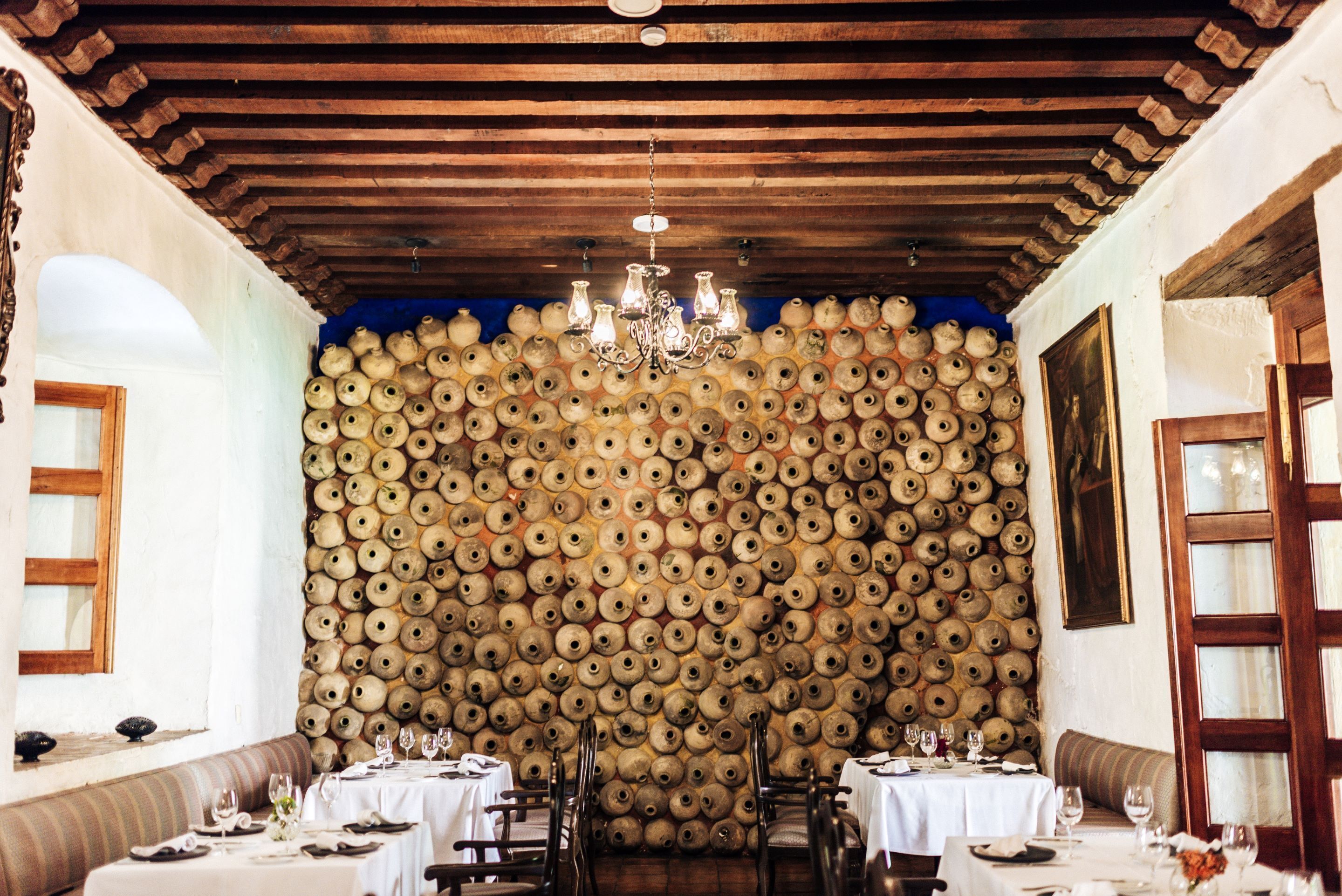 A dining area with tables set for a meal, a wall of wine barrels, and a chandelier.