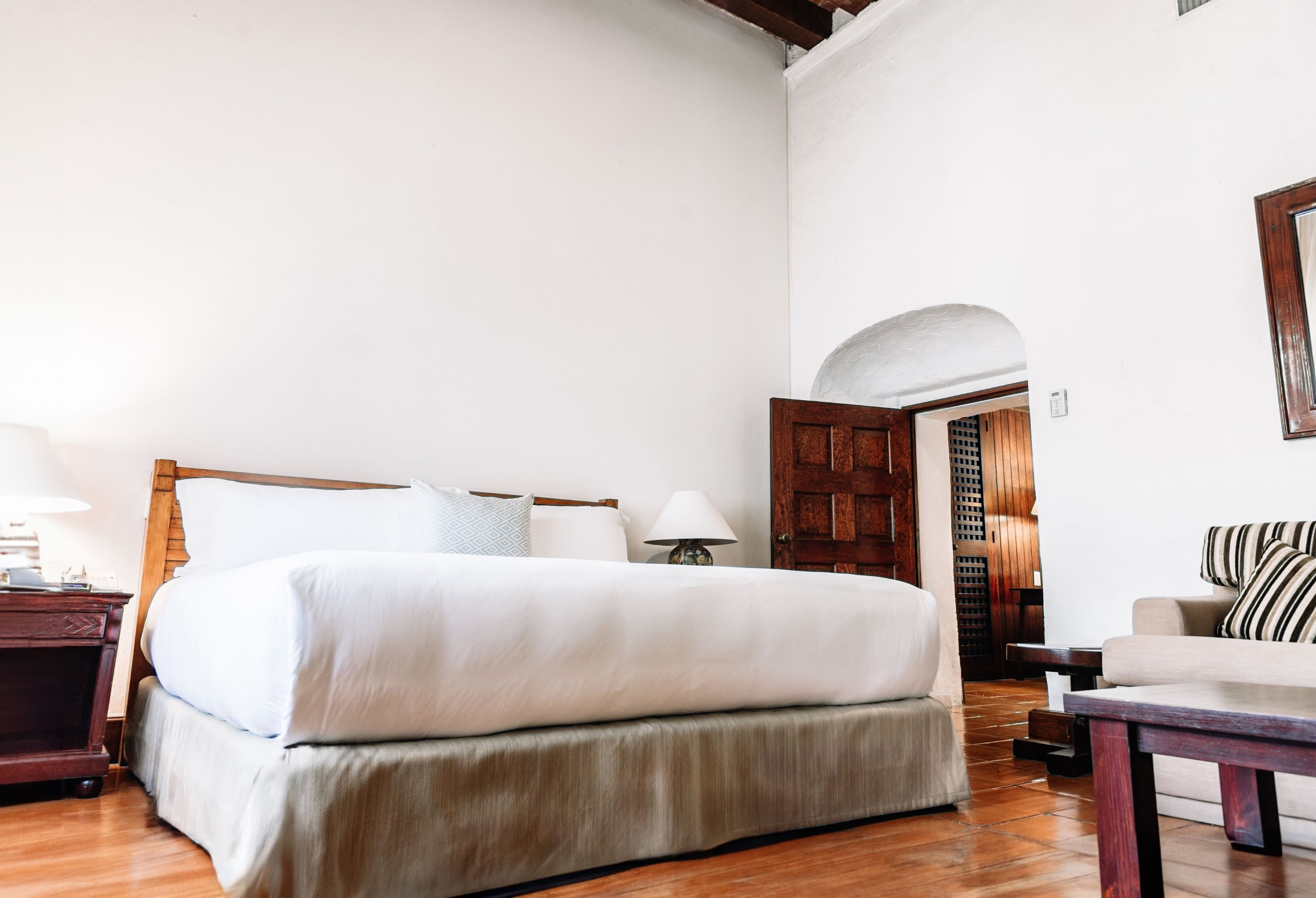A bedroom with a large bed, wooden headboard, bedside tables, a sofa, and a wooden door.