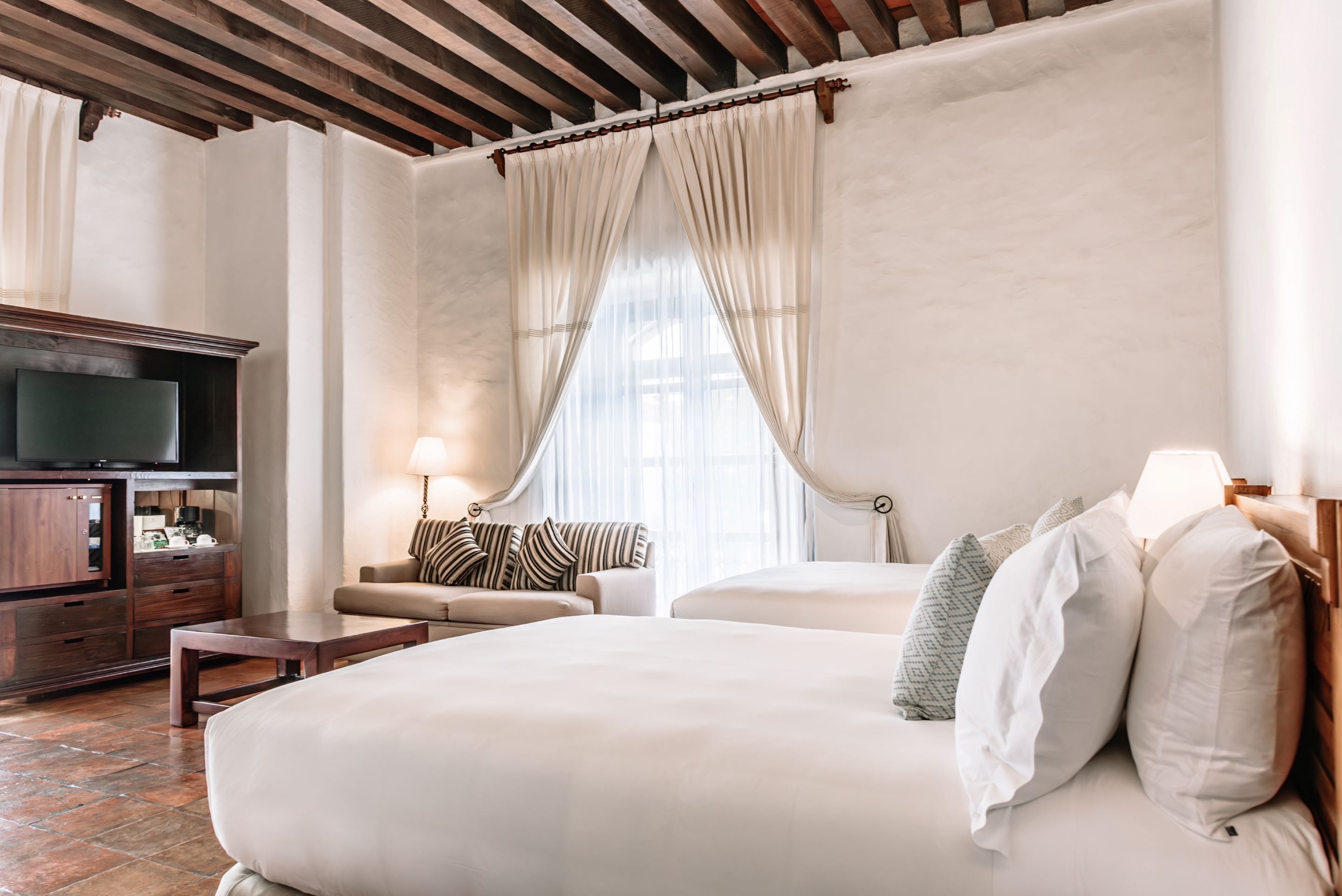 A hotel room with a large bed, a wooden desk, a television, and a sofa.