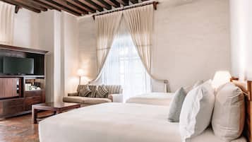 A hotel room with a large bed, a wooden desk, a television, and a sofa.