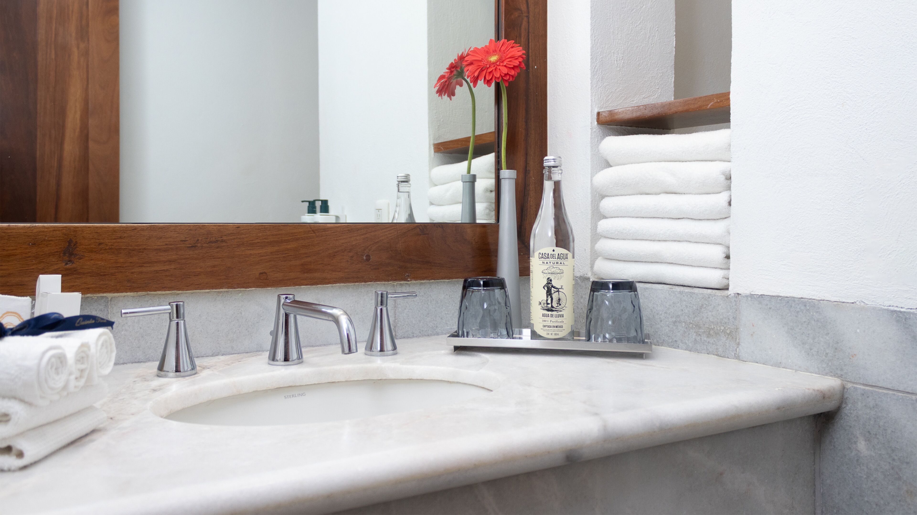 A bathroom with a marble sink, multiple faucets, a mirror, and a bottle of water.
