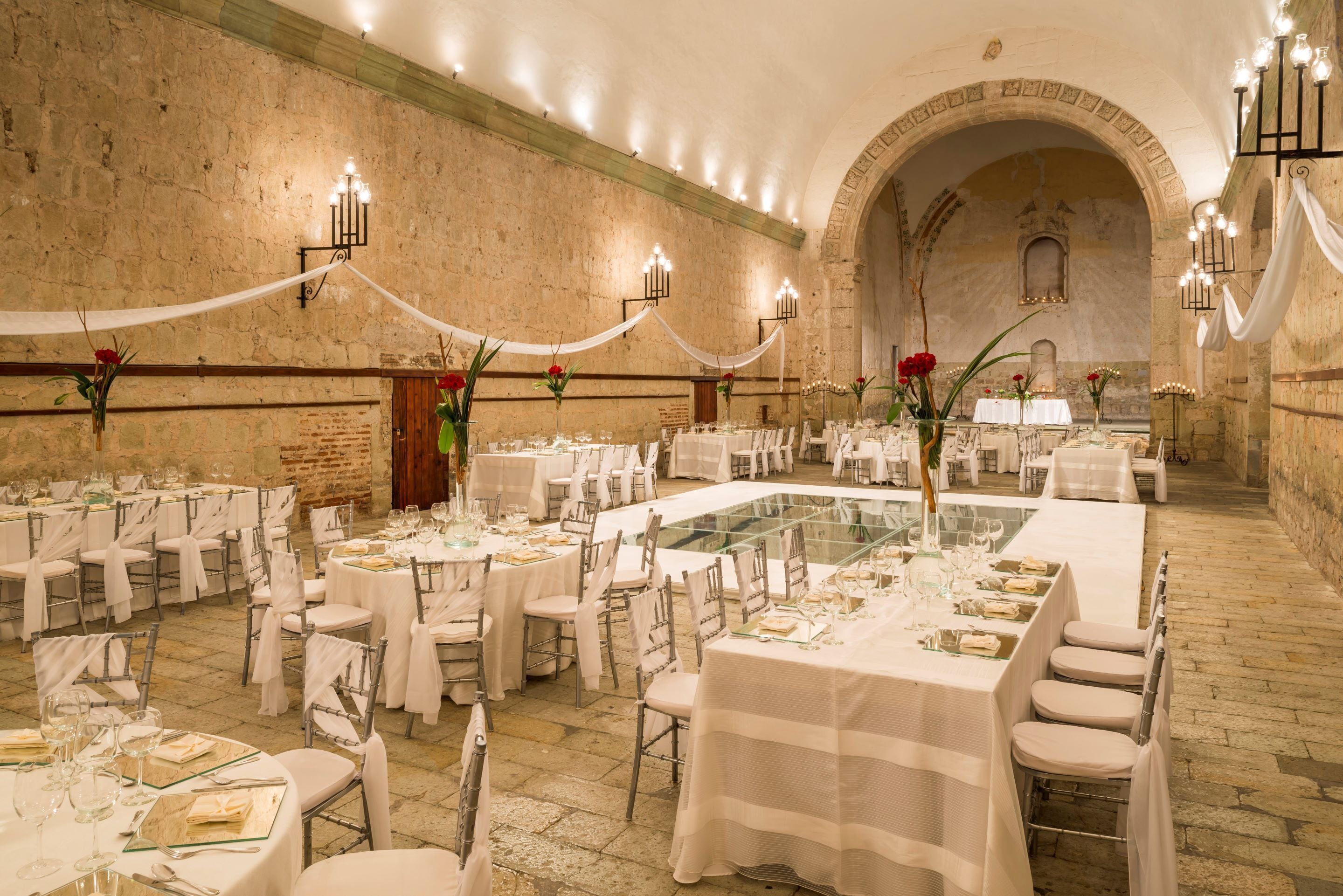 A banquet hall with round tables, white tablecloths, and chandeliers.