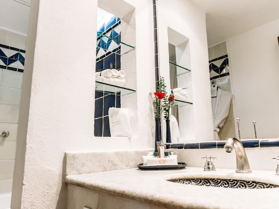 A bathroom with a marble sink, a glass shelf with towels, a mirror, and a window with blue-tiled walls.