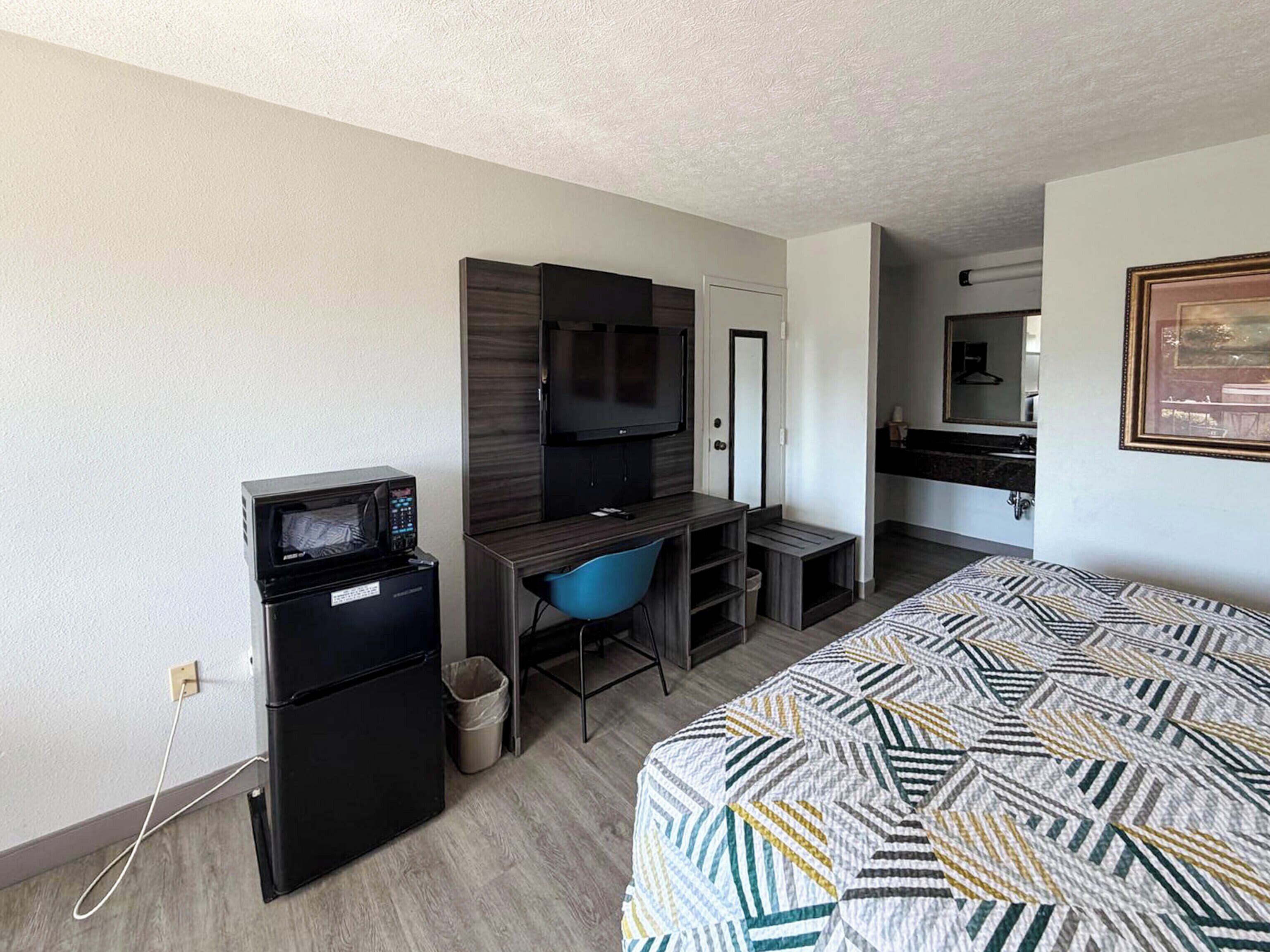 Una habitación de hotel compacta con cama, escritorio con computadora, televisión y una pequeña kitchenette.