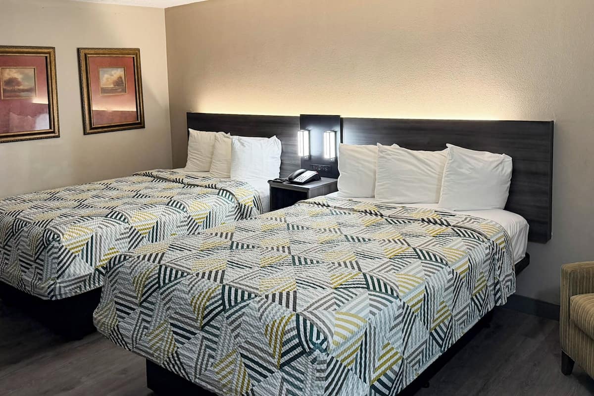 A hotel room with two beds, a nightstand with a phone, and framed pictures on the wall.