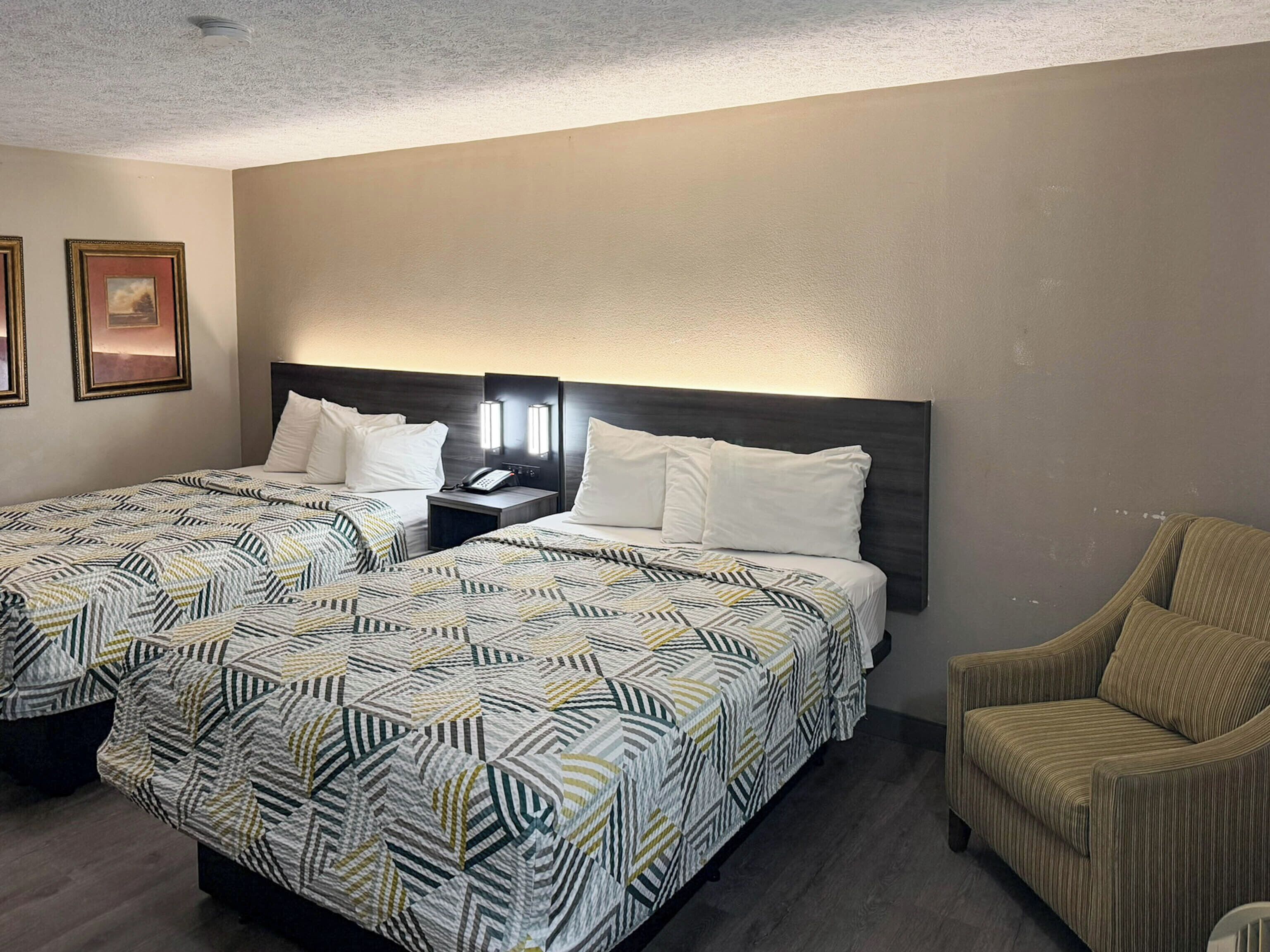A hotel room with two beds, a nightstand with a phone, and a chair.
