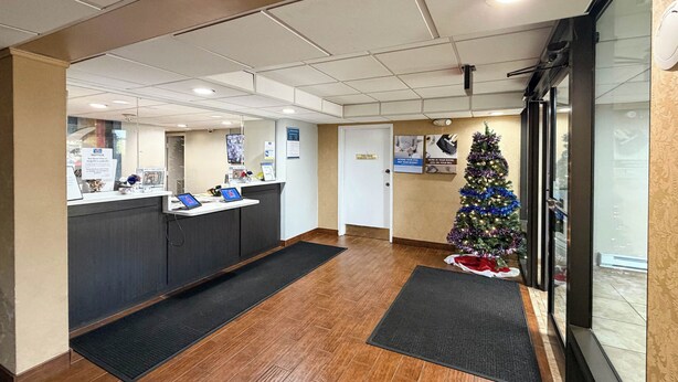 A reception area with a Christmas tree, a counter with computers, and a door with a sign. - Motel 6 Stafford, VA - Quantico (Stafford)