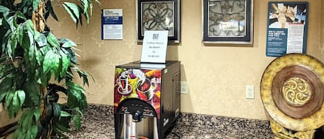 Ein Kaffee-Bereich mit einer Kaffeemaschine, einem Schild mit den Kaffeestunden, gerahmten Bildern an der Wand und einer dekorativen Platte.