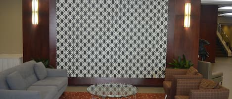 Un vestíbulo con una pared estampada, un sofá gris, una mesa redonda de vidrio y sillones marrones.