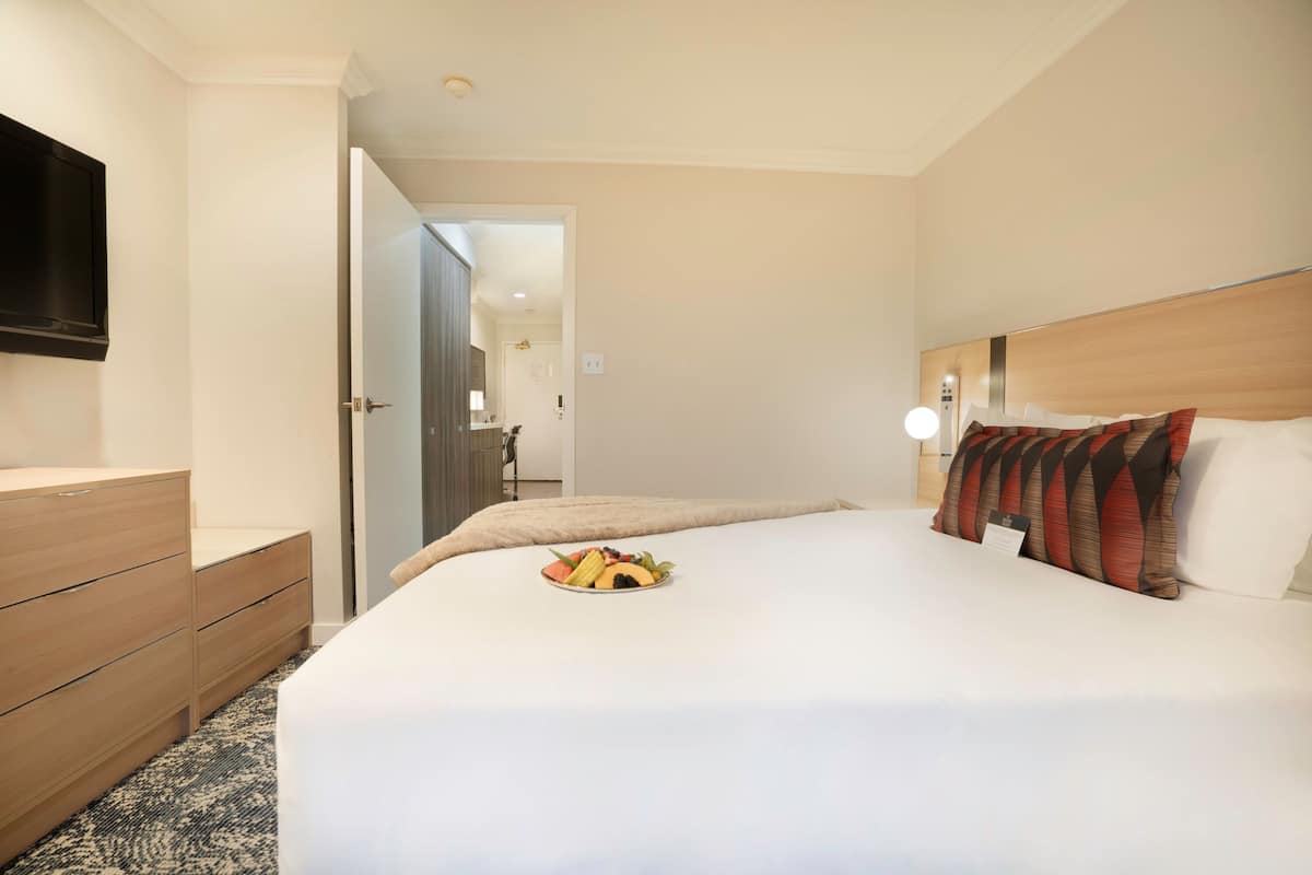 A hotel room with a bed, a TV, a dresser, and a breakfast plate on the bed.