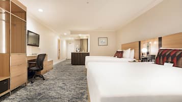 Quarto de hotel com cama, escrivaninha, cadeira, televisão e um espaço de banheiro pequeno.