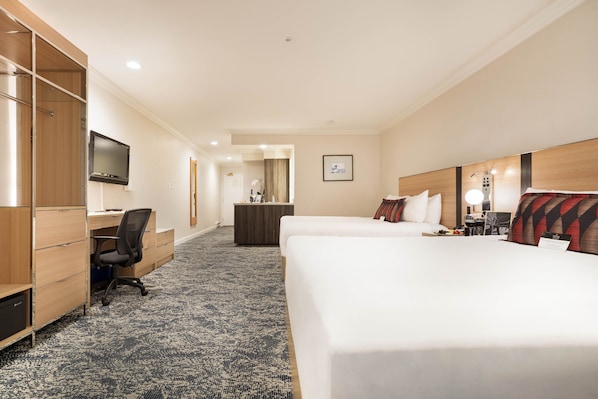 A hotel room with a bed, desk, chair, TV, and a small bathroom area.