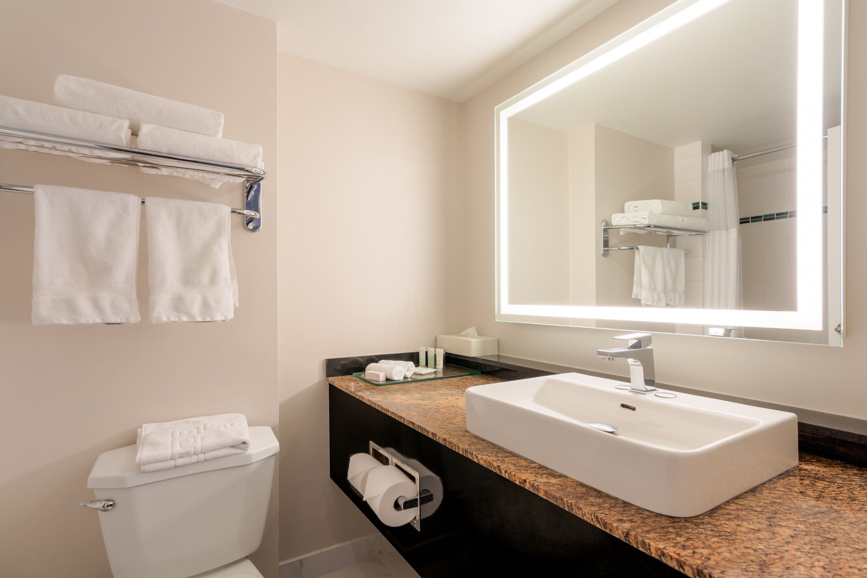 A modern bathroom with a white sink, a large mirror, and a towel rack with multiple towels.