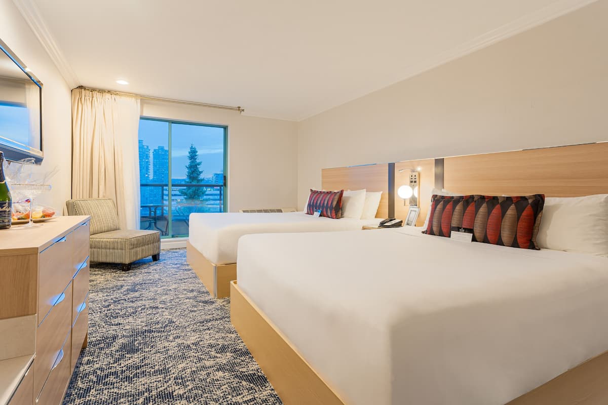 A hotel room with two beds, a desk, a chair, and a large window with a city view.