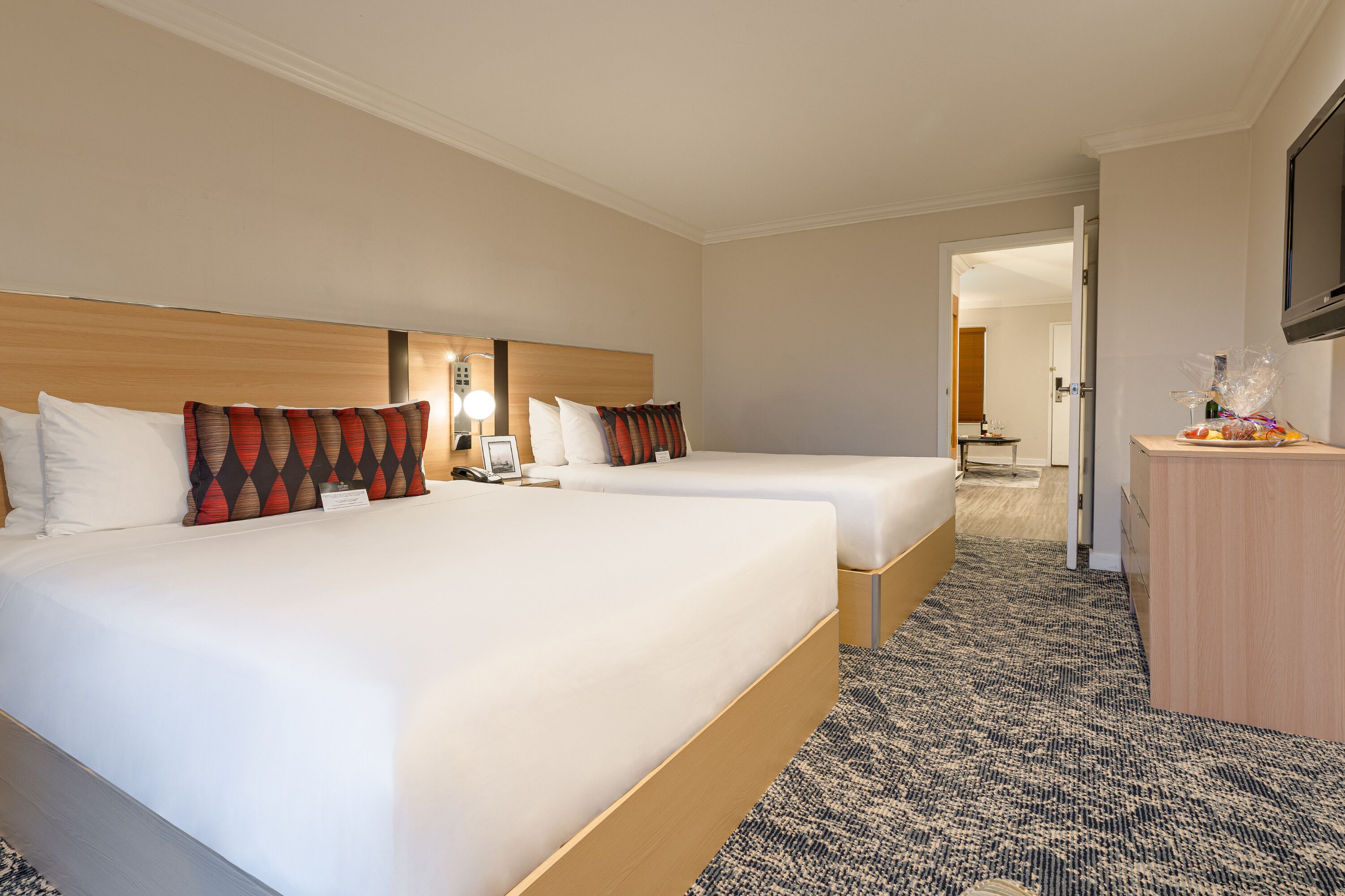 A hotel room with two beds, a wooden headboard, a flat-screen TV, and a desk with a lamp.