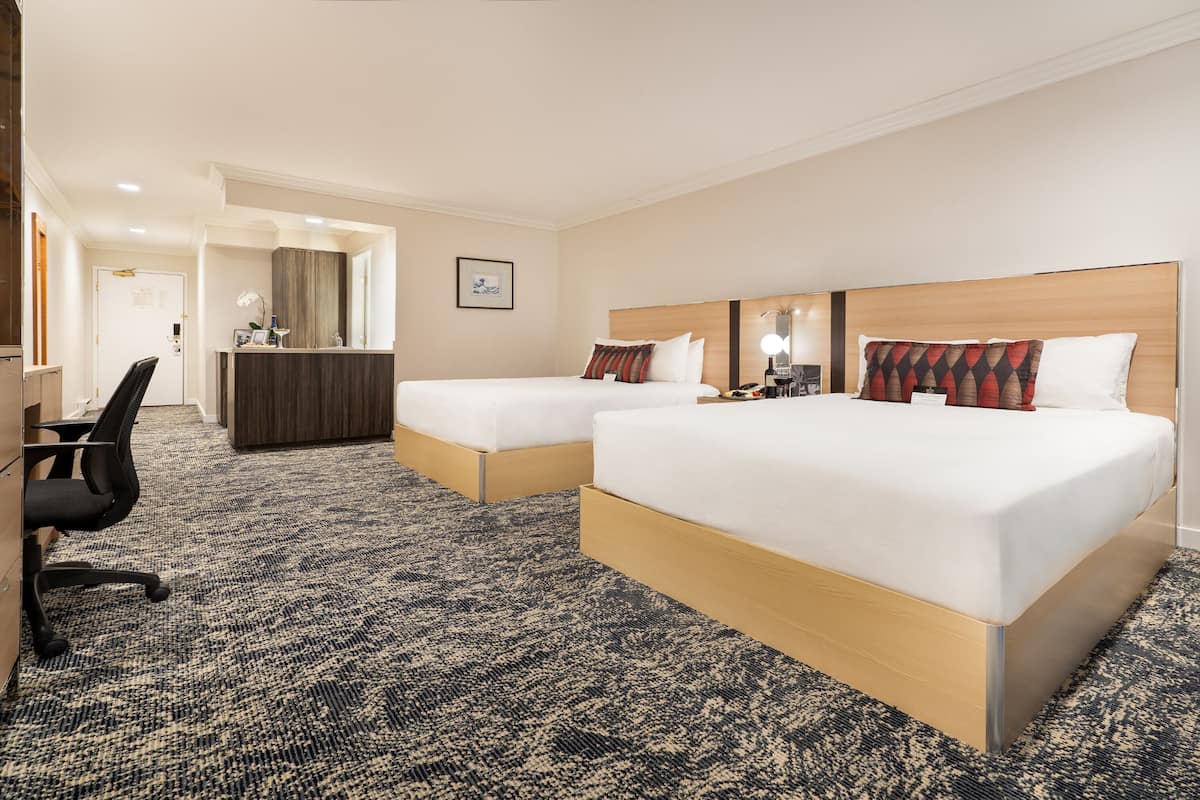 A hotel room with two beds, a desk, and a chair.