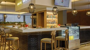 A modern bar area with a counter, bar stools, and a refrigerated display. - Fiesta Inn Monterrey Valle (San Pedro Garza García)