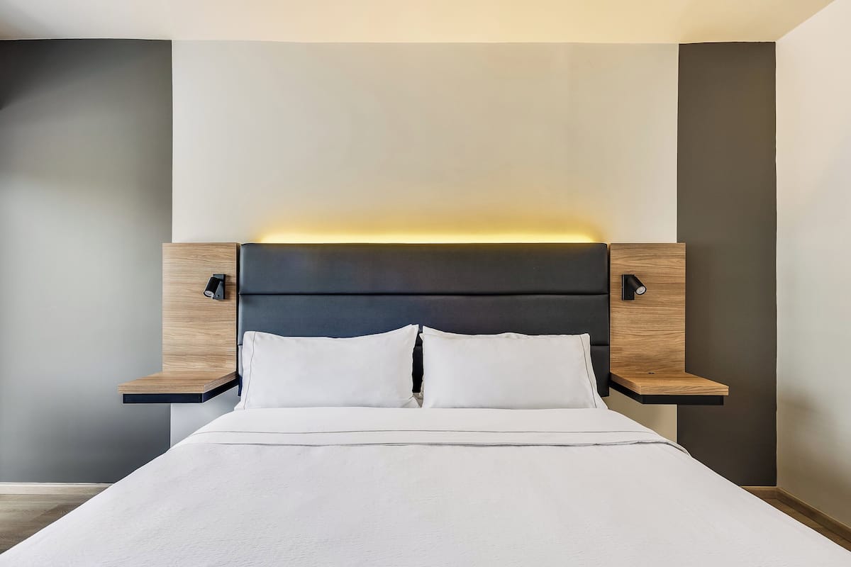 A modern bed with a headboard, bedside tables, and a wall-mounted light.