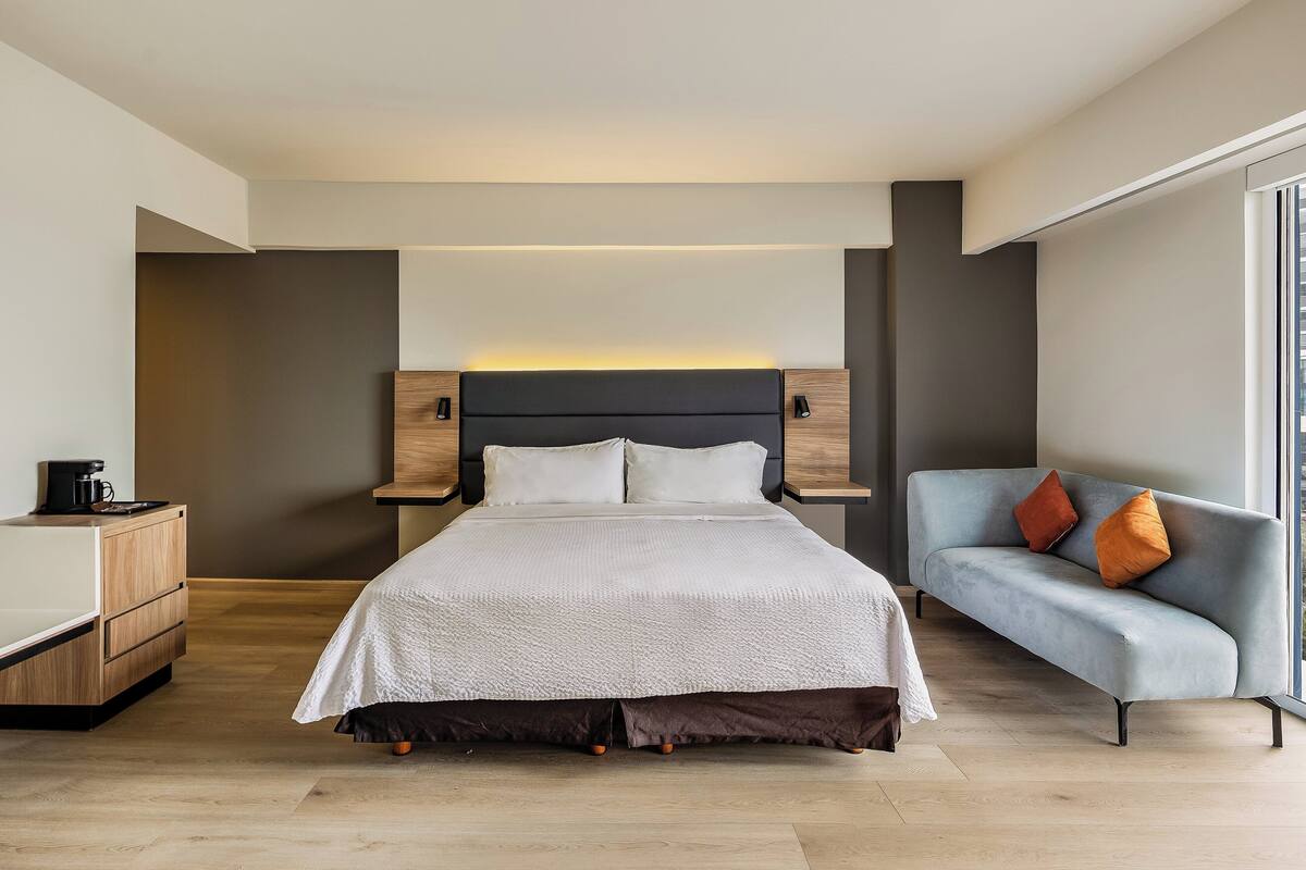 A modern hotel room with a large bed, a sofa, a coffee table, and a desk.