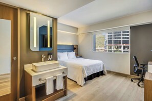 A modern hotel room with a large bed, a bathroom with a vanity, and a window with a view of the outside. - Fiesta Inn Monterrey Valle (San Pedro Garza García)