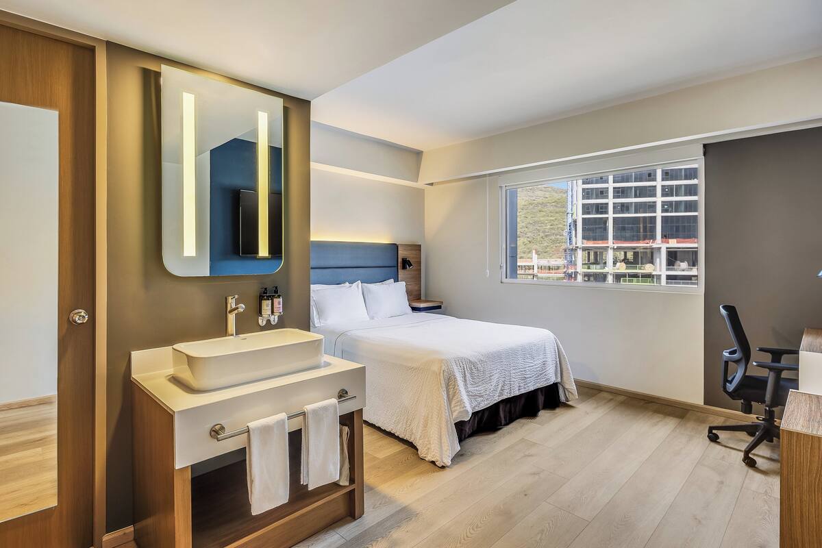 A modern bedroom with a large bed, a bedside table, a desk, and a window with a view.