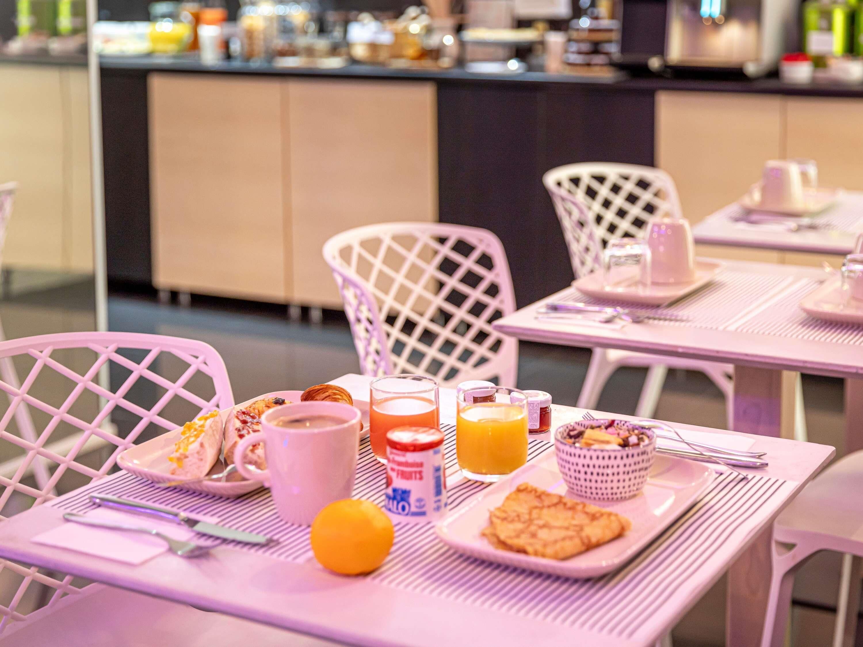 Een ontbijtsetting met een tafel, stoelen en diverse etenswaren, waaronder een croissant, sinaasappelsap en een kom ontbijtgranen.