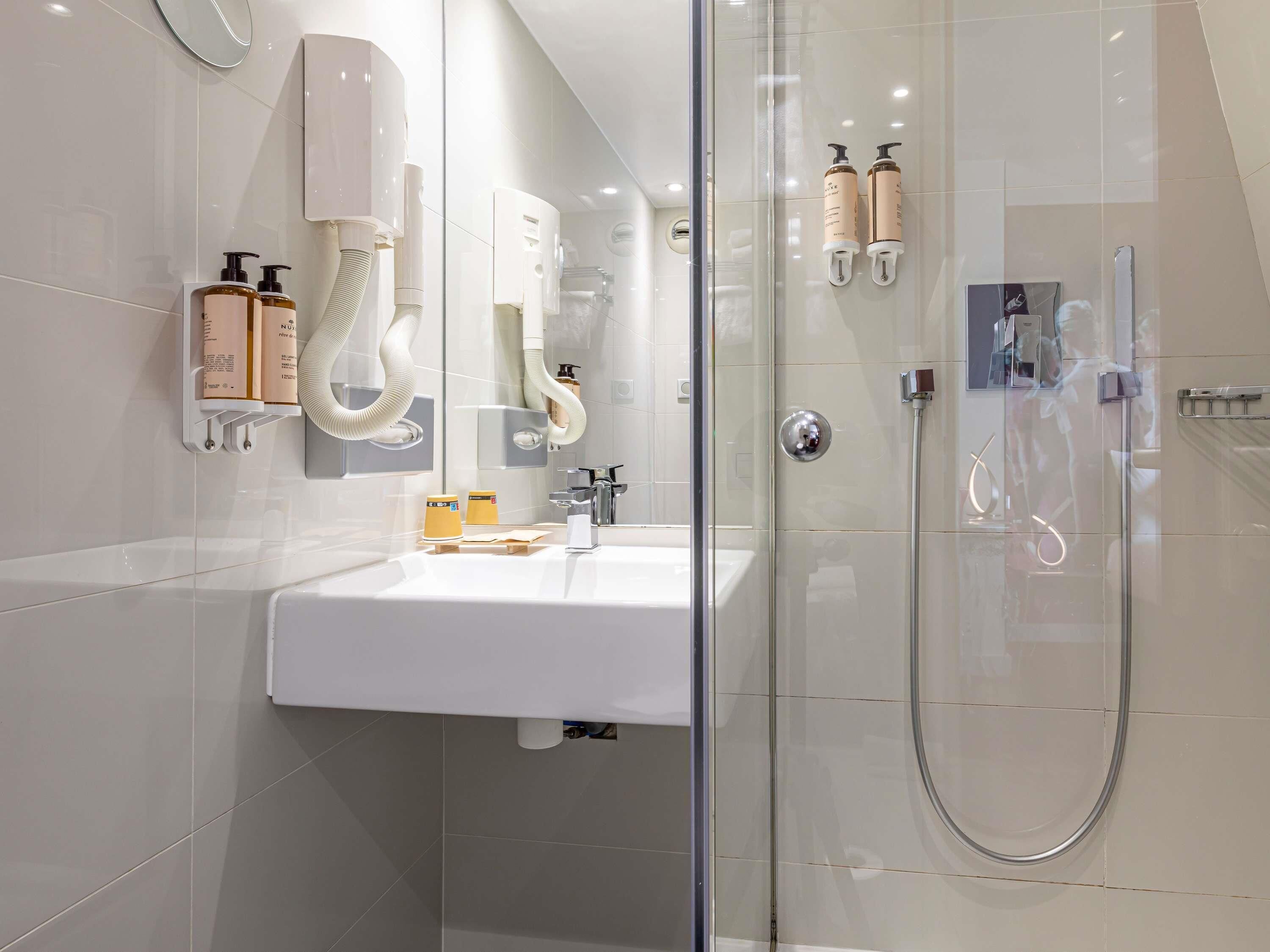 A modern bathroom with a glass shower enclosure, a white sink, and toiletries mounted on the wall.