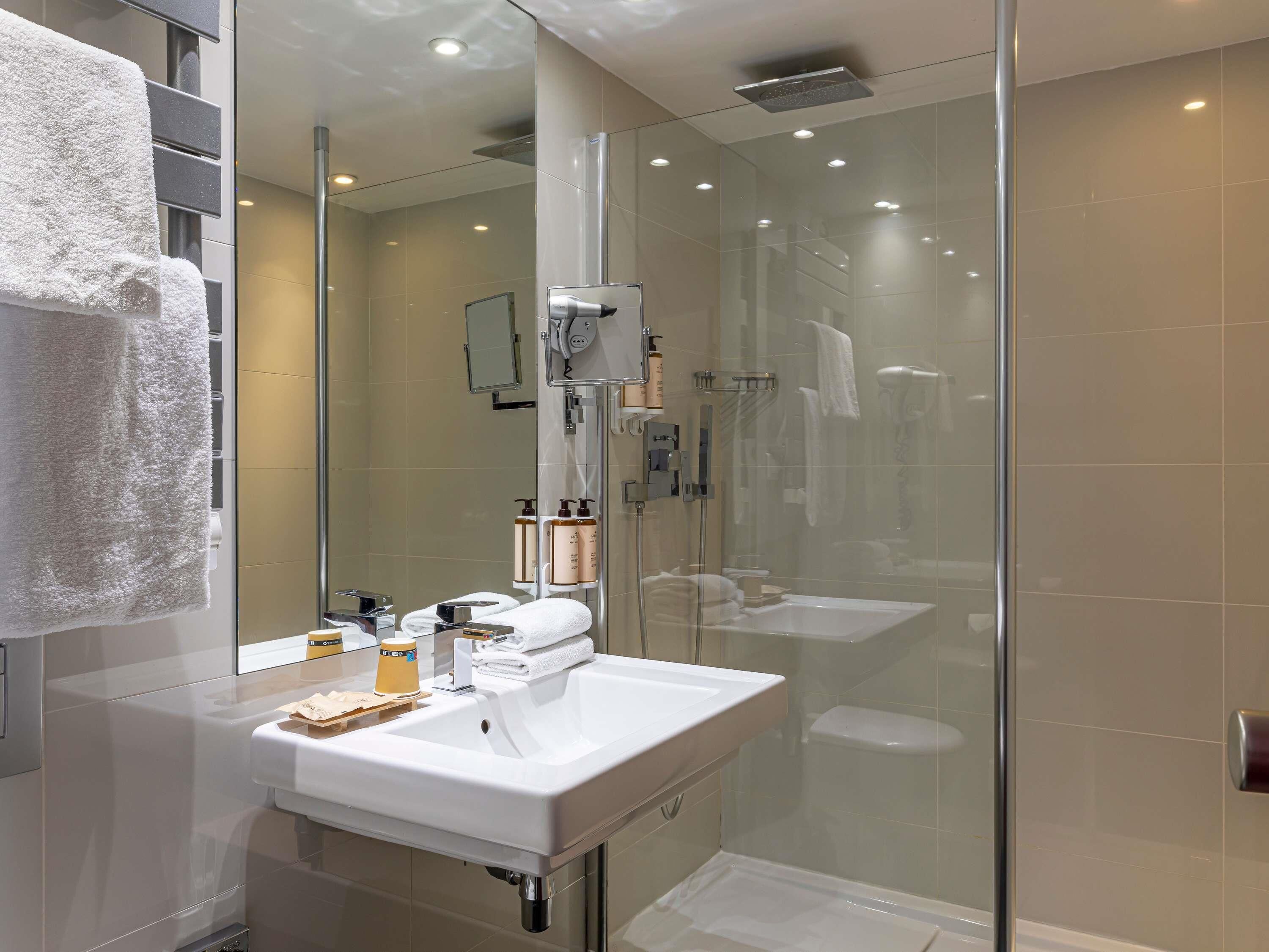 A modern bathroom with a glass shower enclosure, a white sink, and a mirror.