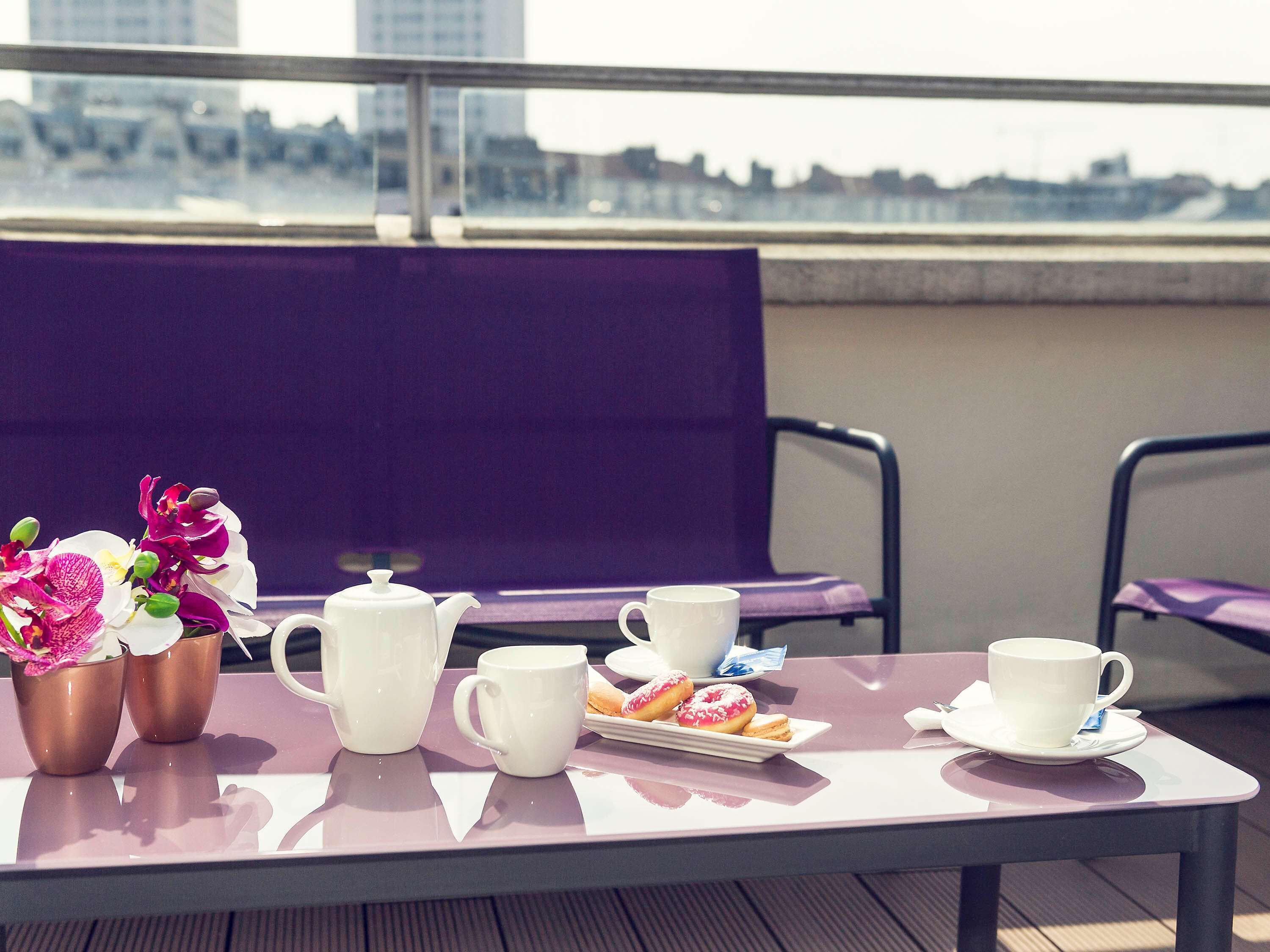 A table with a teapot, cups, and pastries on a balcony with a city view.