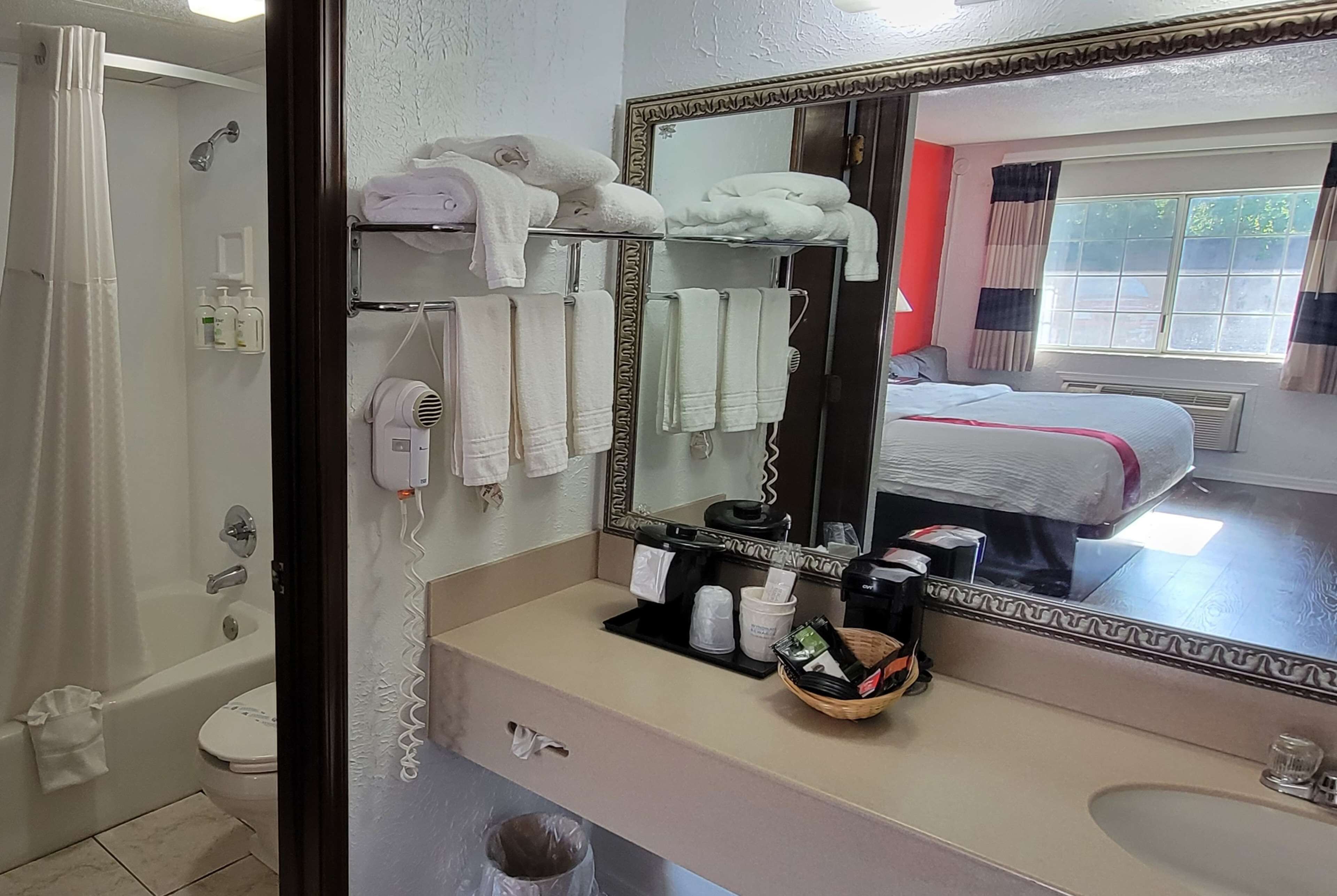 A bathroom with a large mirror, a bathtub, a toilet, and a sink with toiletries.