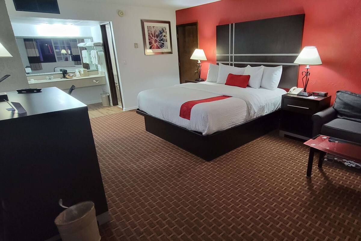 A hotel room with a large bed, bedside tables with lamps, a desk, and a mirror.