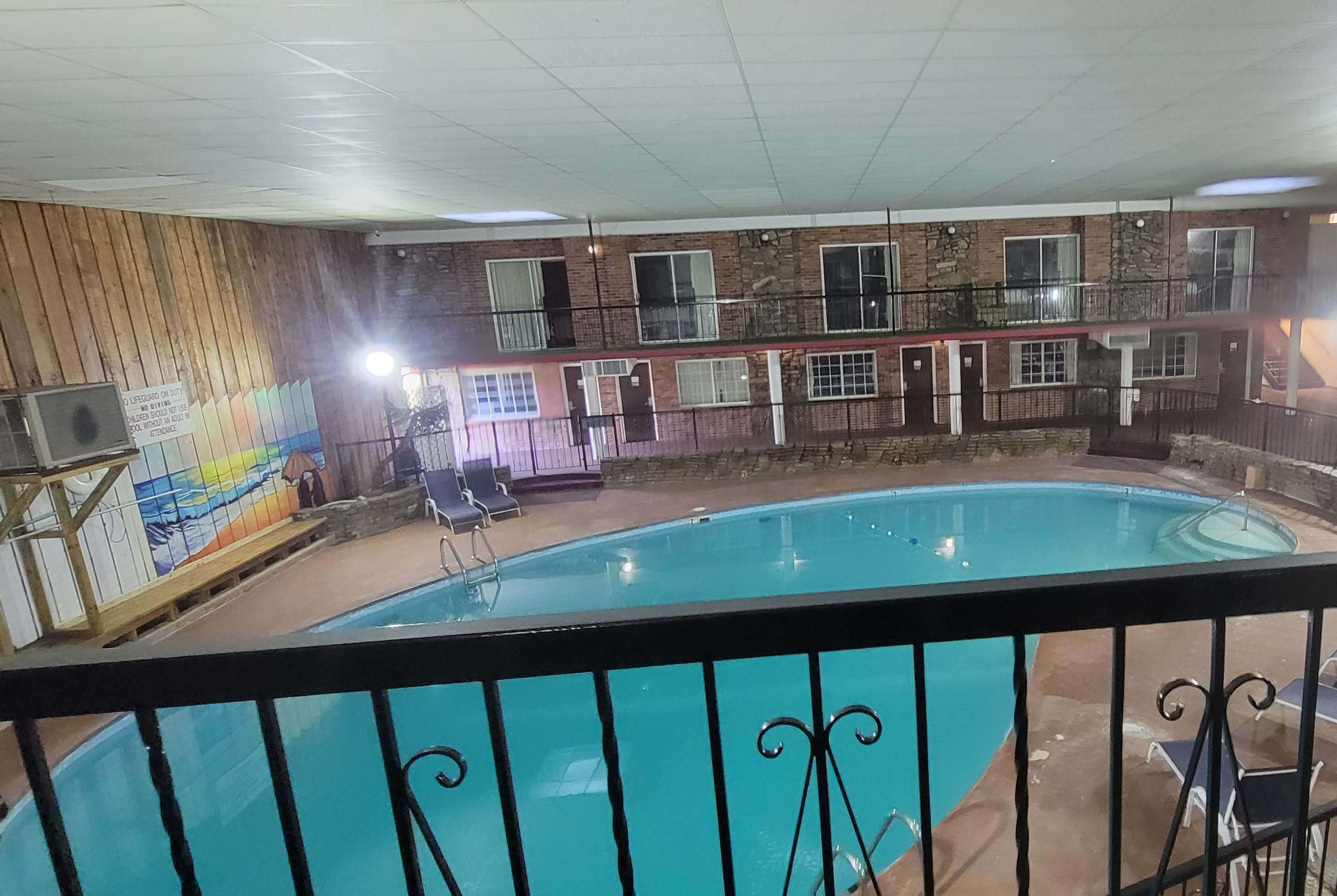 Una piscina interior con un mural de madera, un balcón con barandilla y un edificio de varios niveles al fondo.
