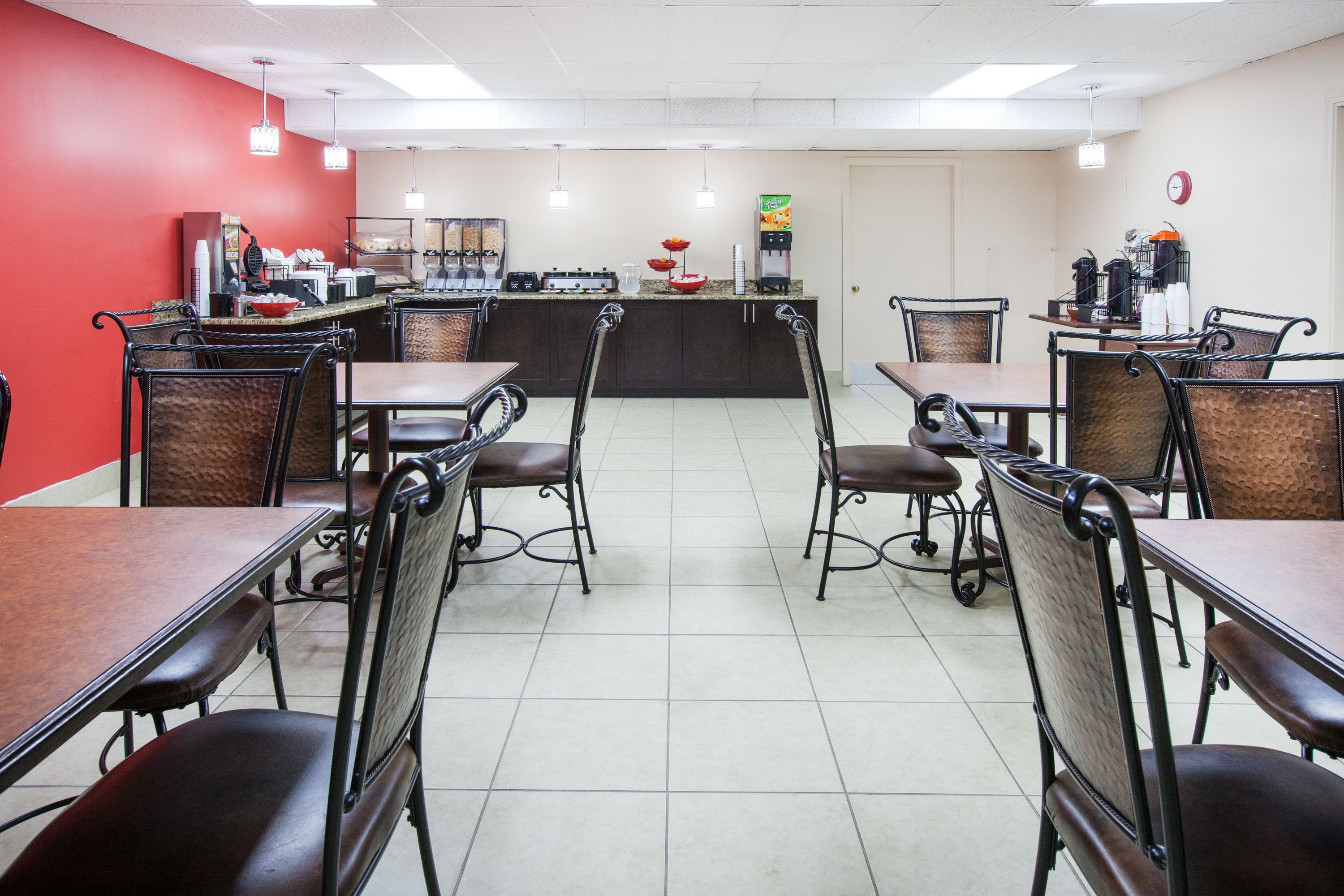 A restaurant with multiple tables and chairs, a counter with a coffee machine, and a red wall.