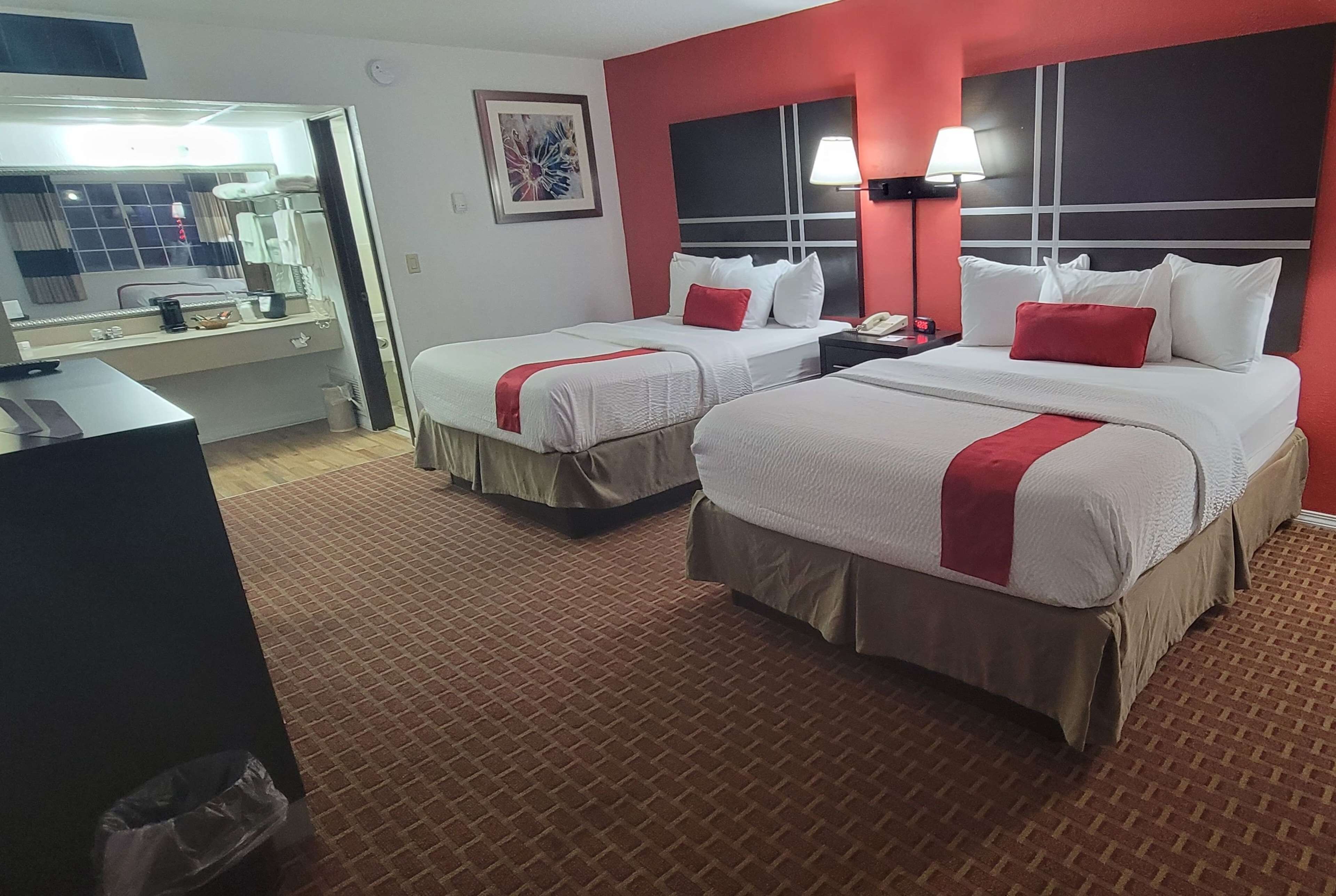 Camera d'albergo con due letti, una scrivania, uno specchio e un pavimento tappezzato di moquette rossa.