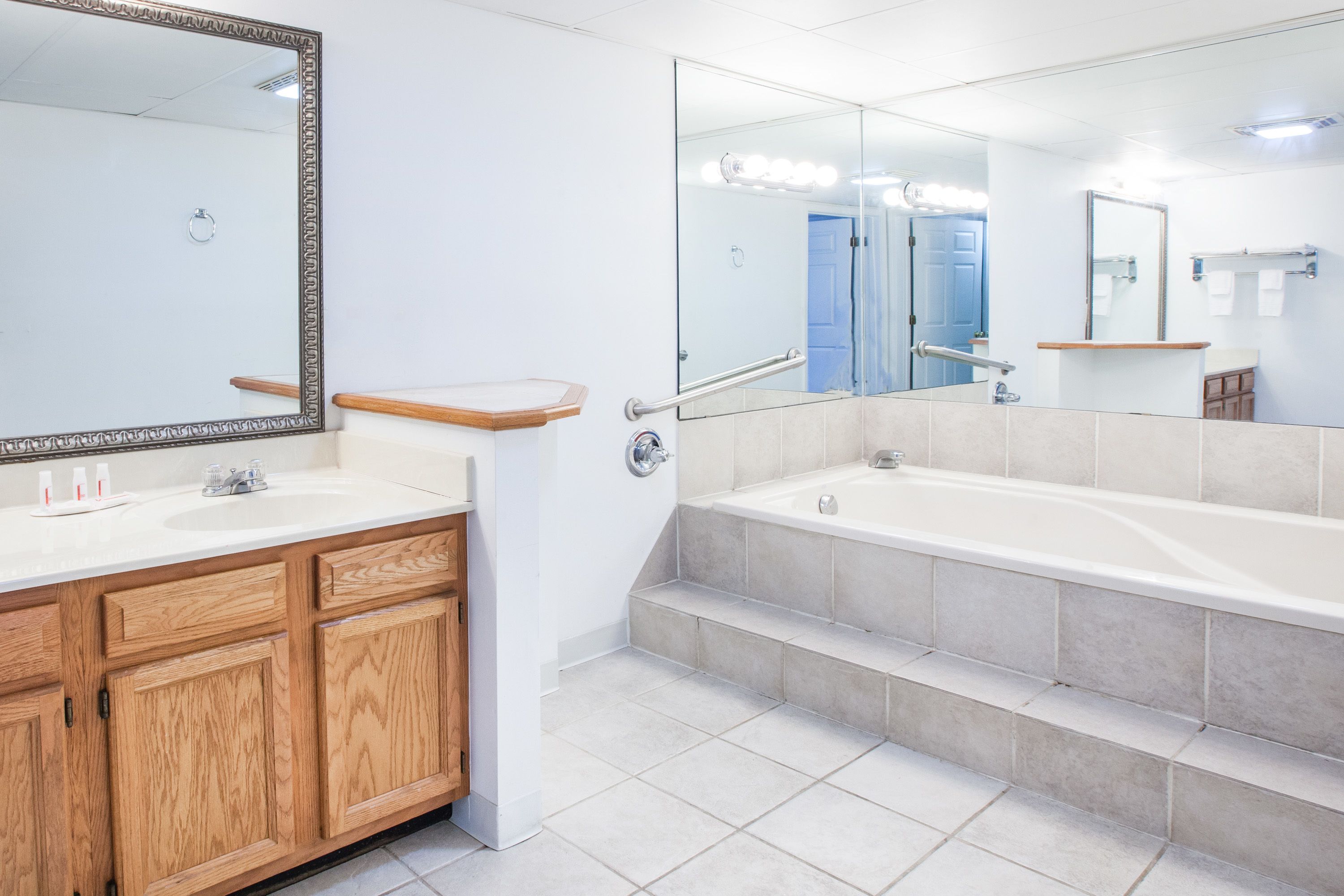 A modern bathroom with a wooden vanity, a large mirror, a bathtub, and a separate sink.