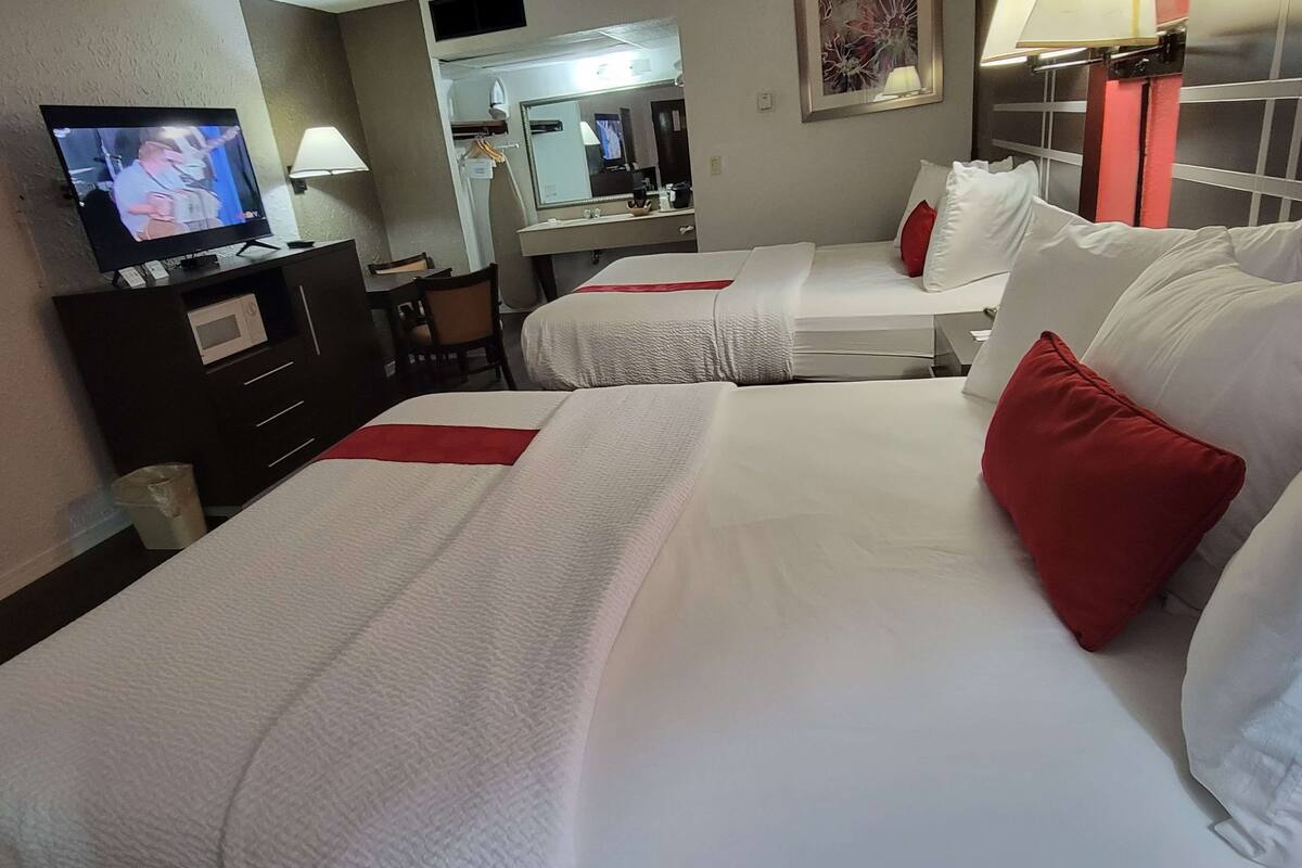 A hotel room with two beds, a TV, a desk with a lamp, and a mirror.