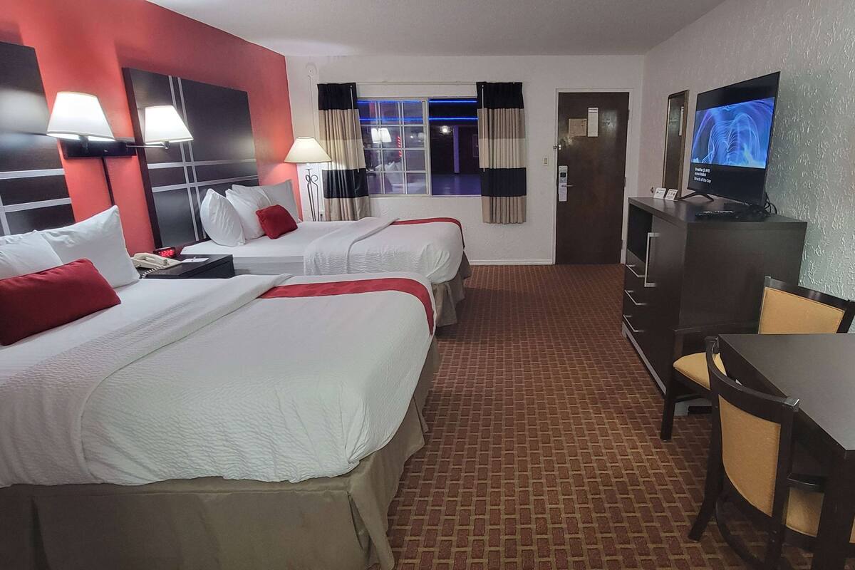 A hotel room with two beds, a TV, a desk, and a chair.