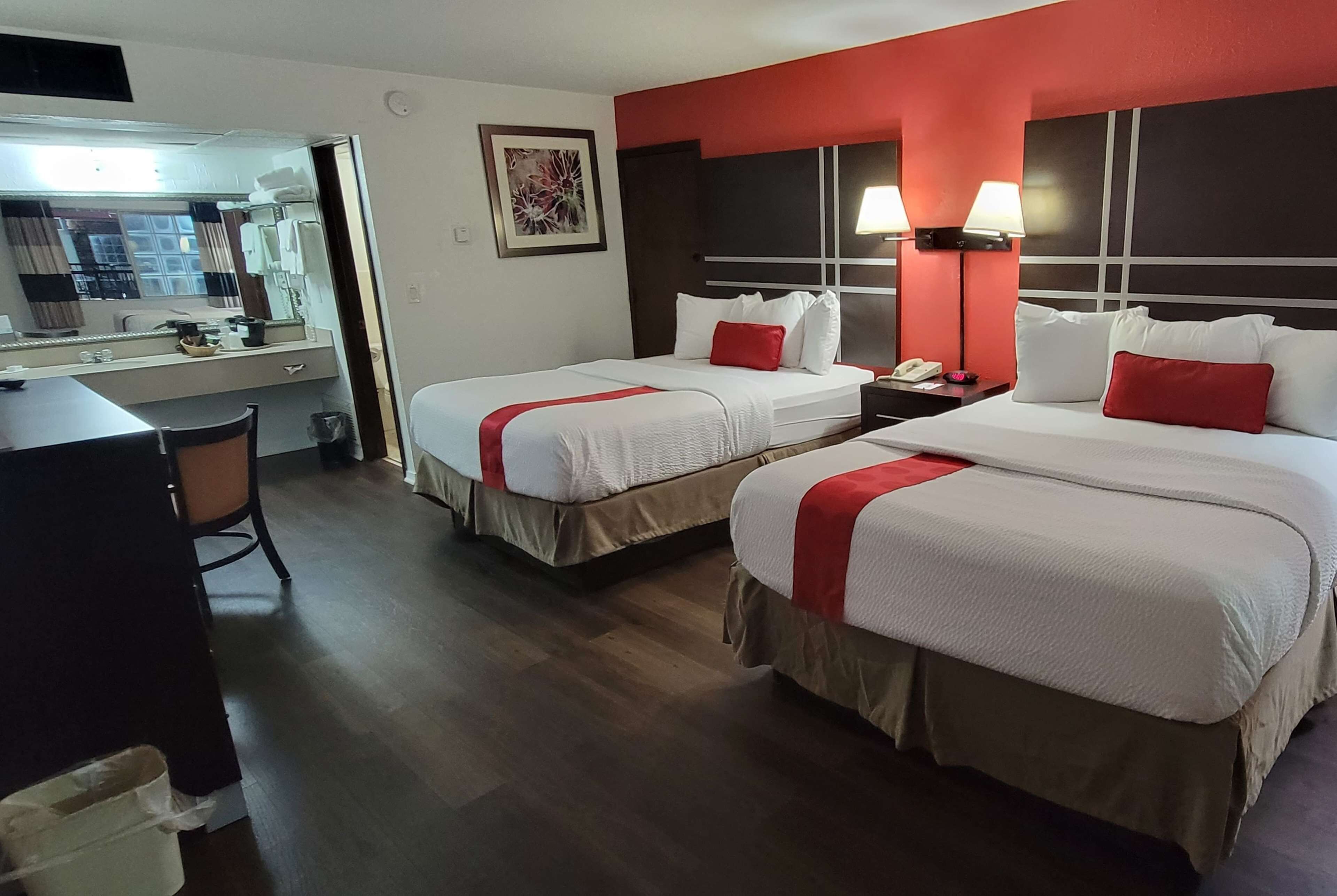 A hotel room with two beds, a desk, a chair, a mirror, and a small bathroom.