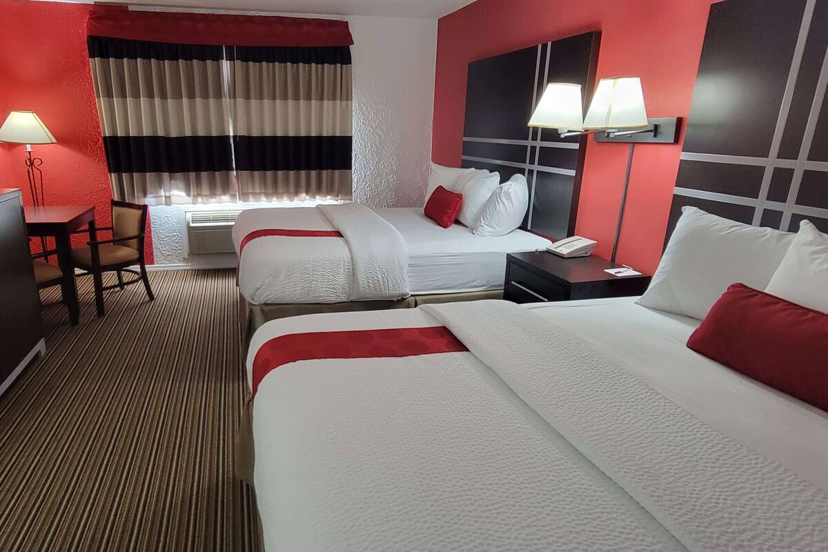 A hotel room with two beds, a desk, a chair, a lamp, and a window with curtains.