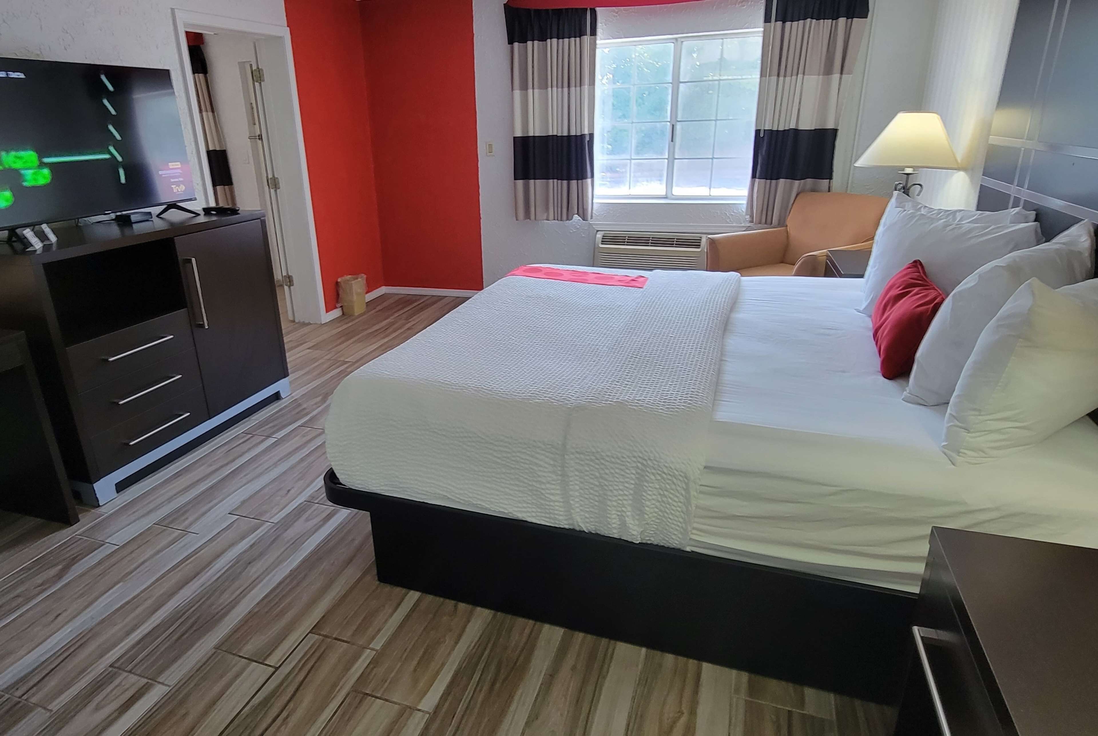Ein Hotelzimmer mit Bett, Fernseher auf einem Schrank, einem Sessel und einem Fenster mit Vorhängen.