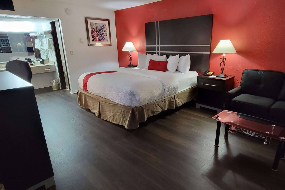 A hotel room with a large bed, two bedside lamps, a desk with a chair, and a red accent wall.