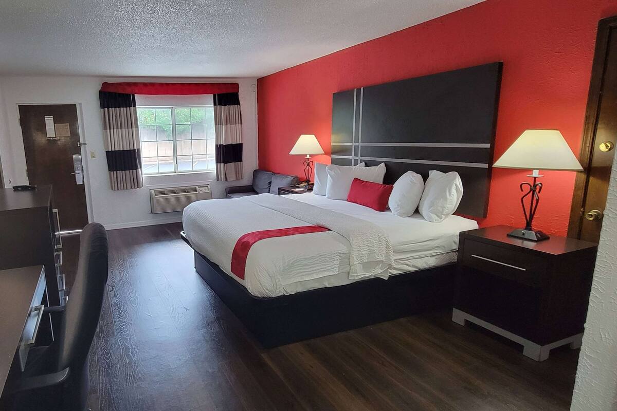 A hotel room with a large bed, two bedside tables with lamps, a desk, and a chair.