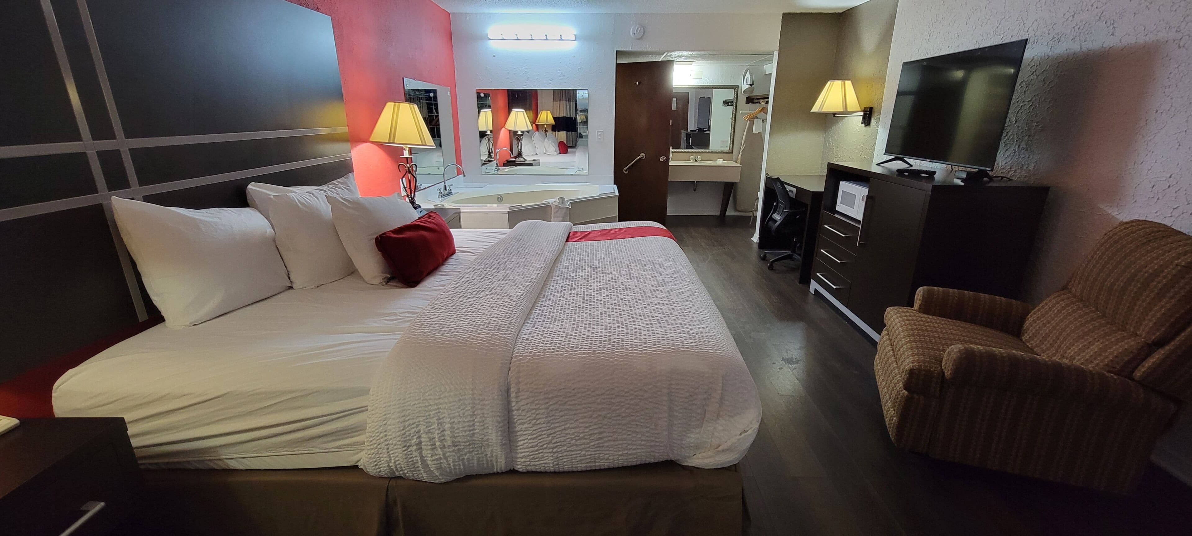 A hotel room with a large bed, a desk, a TV, and a chair.