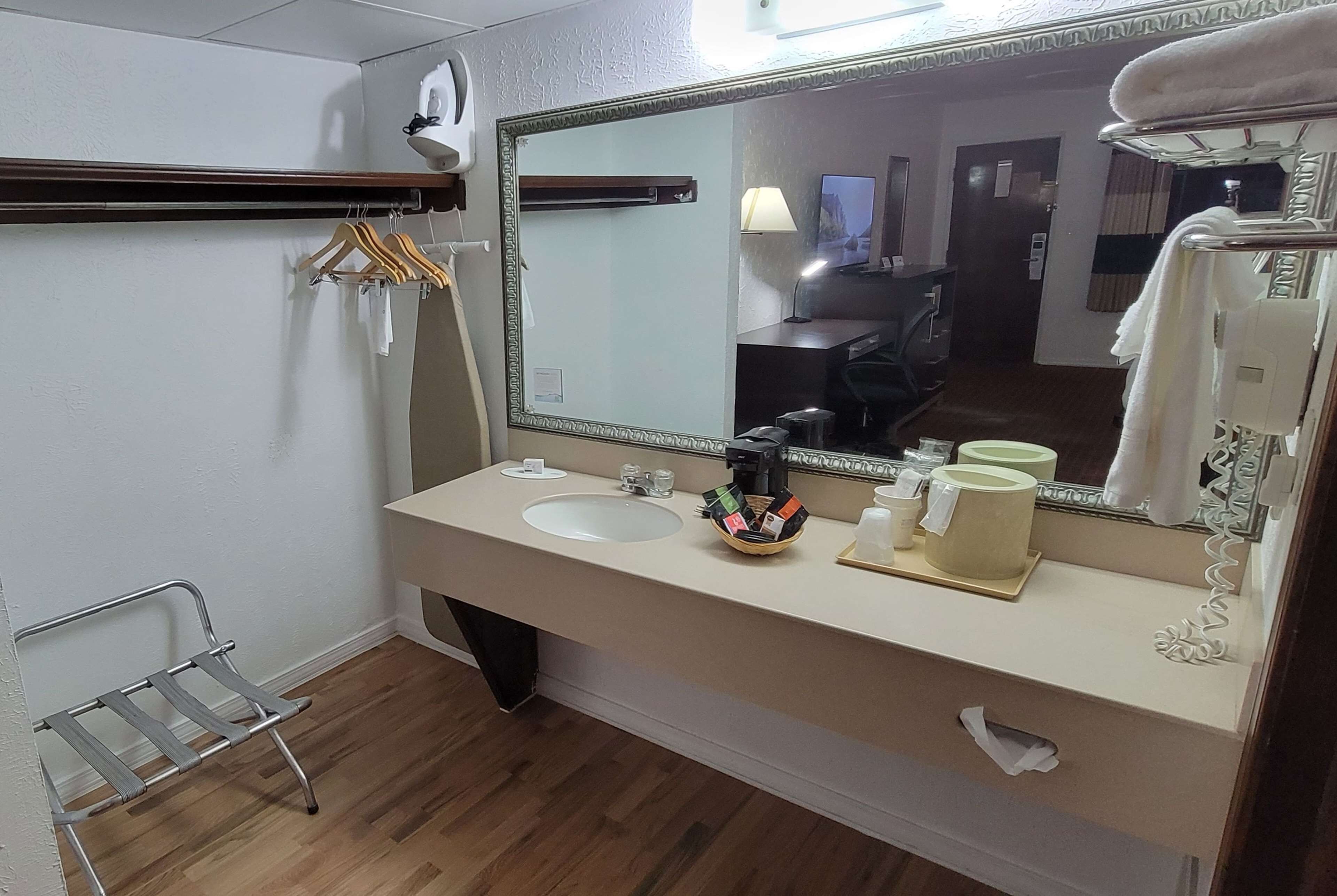 A hotel bathroom with a sink, mirror, towel rack, and a small shelf with toiletries.