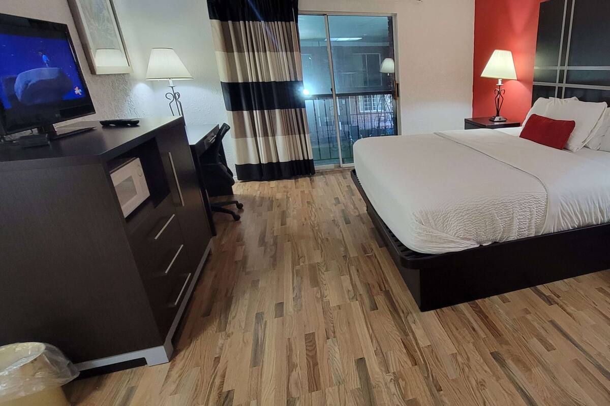 A hotel room with a bed, a desk with a TV, a lamp, and a view of the outside.