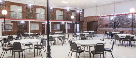A spacious indoor dining area with multiple round tables and chairs, a stone accent wall, and a balcony with railings.