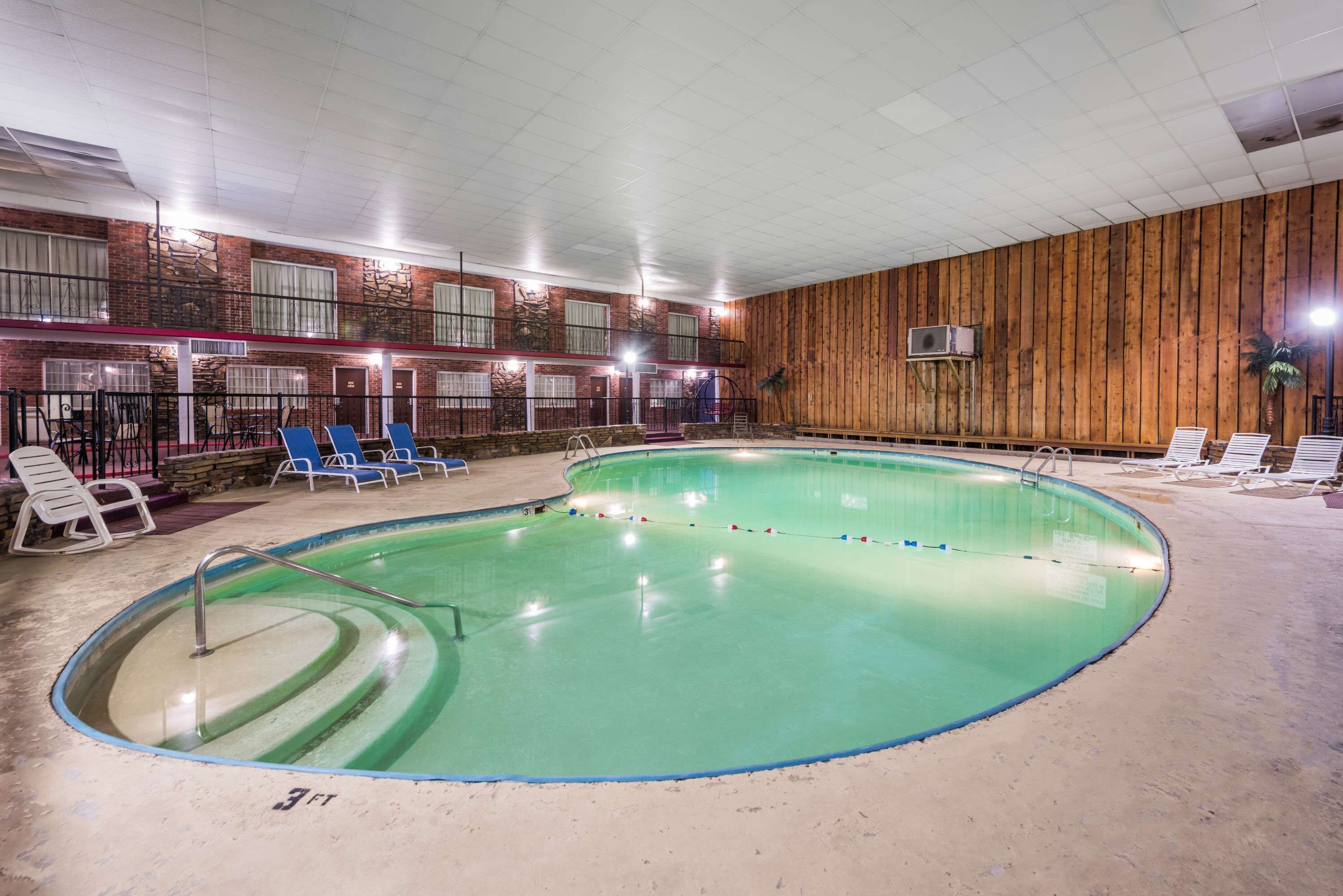 An indoor swimming pool with blue lounge chairs, a brick wall, and a wooden panel wall.