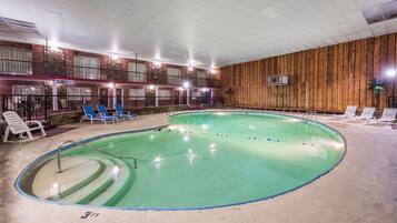 An indoor swimming pool with blue lounge chairs, a brick wall, and a wooden panel wall.